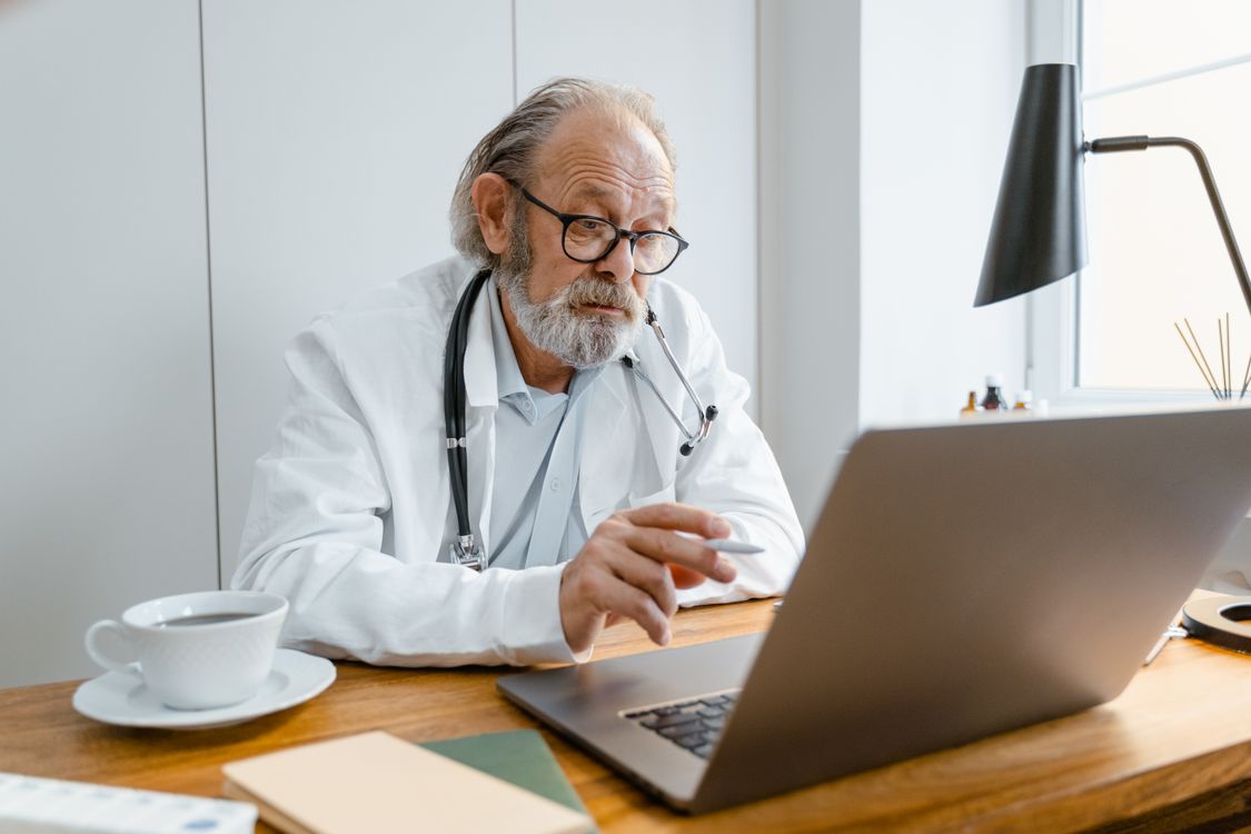 An older doctor reviewing information on a laptop
